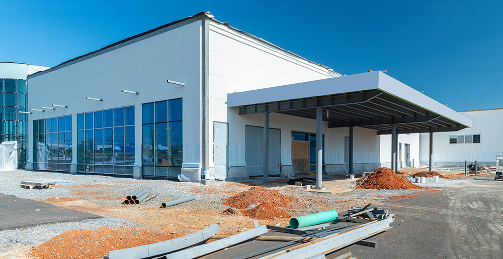 A commercial building under construction, with pipes & piles of dirt in the parking lot.